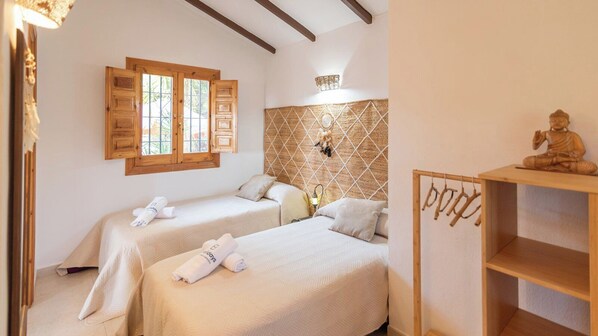 A room with two beds, a wooden headboard, a small shelf with a statue, and a window with shutters. - Casa Surrender Cómpeta by Ruralidays (Málaga)