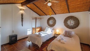 A cozy room with two beds, a wooden ceiling, a small stove, and decorative wall mirrors. - Casa Surrender Cómpeta by Ruralidays (Málaga)