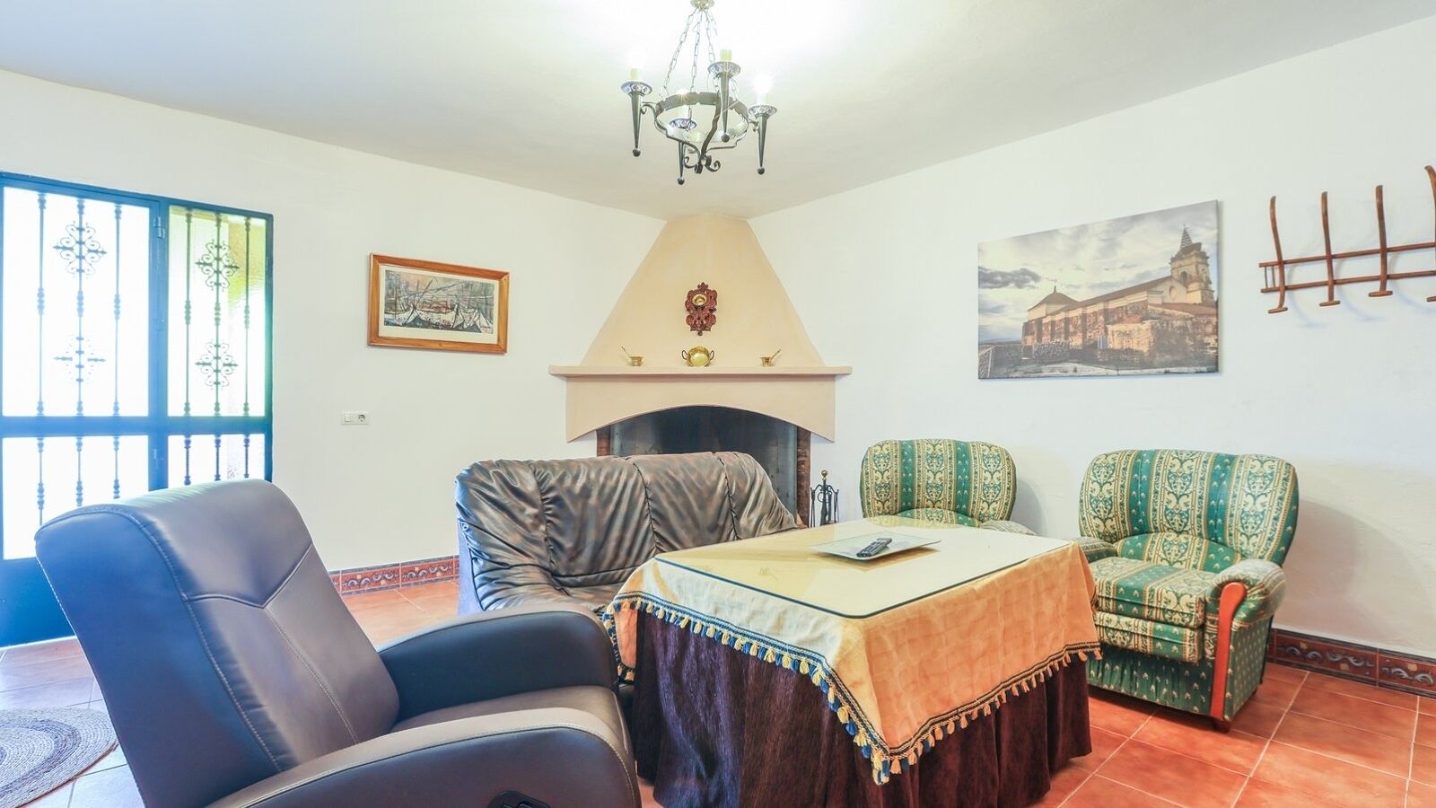 Een woonkamer met een open haard, leren fauteuils, een tafel met tafelkleed en een kroonluchter.