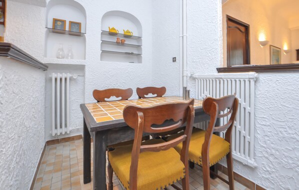 A dining area with a table and chairs, white textured walls, a radiator, and shelves with decorative items.