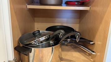 A kitchen cabinet with two stainless steel pots and a red frying pan on a shelf.