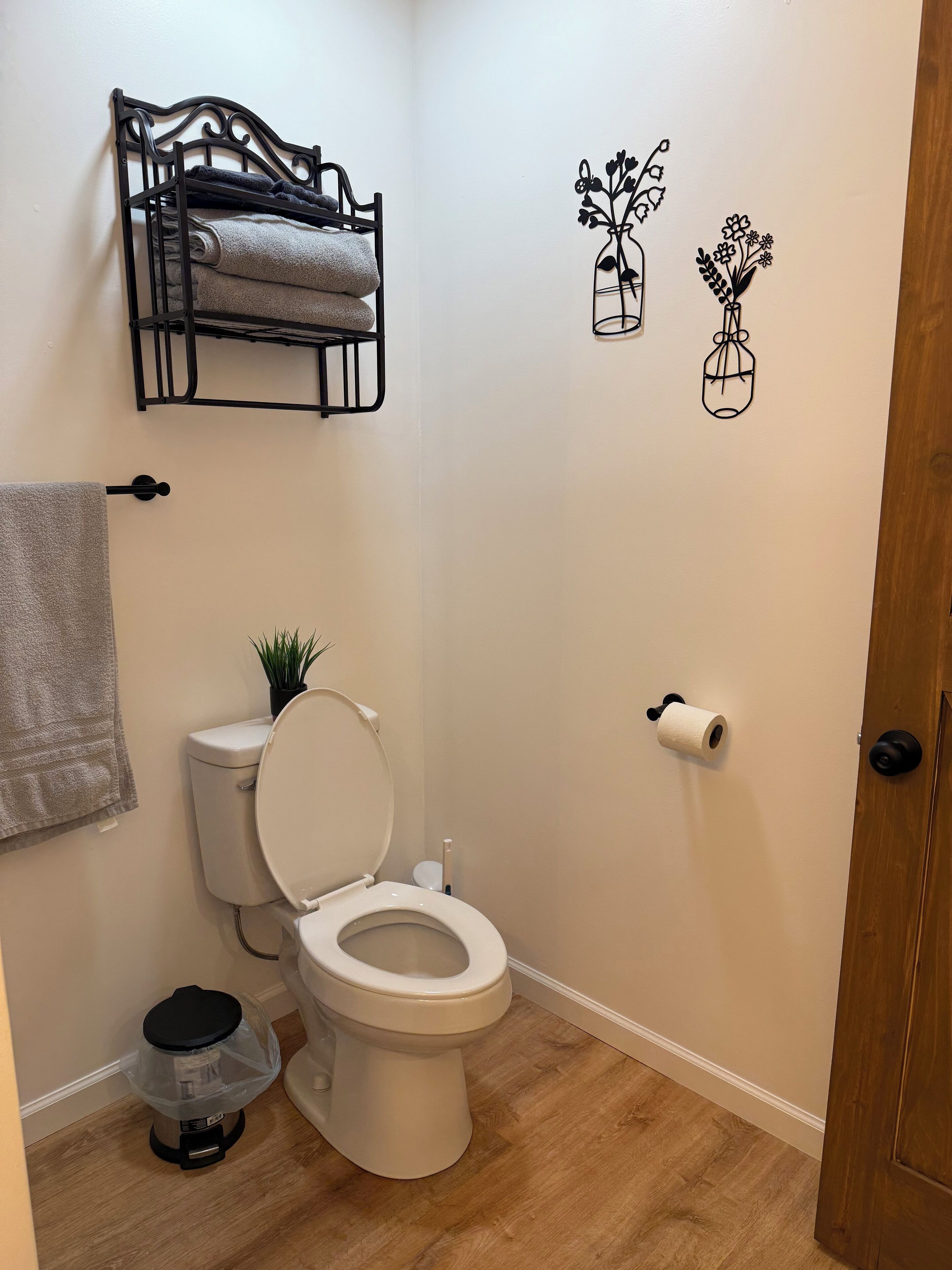 Et badeværelse med toilet, håndklædestang, skraldespand og toiletpapirholder.