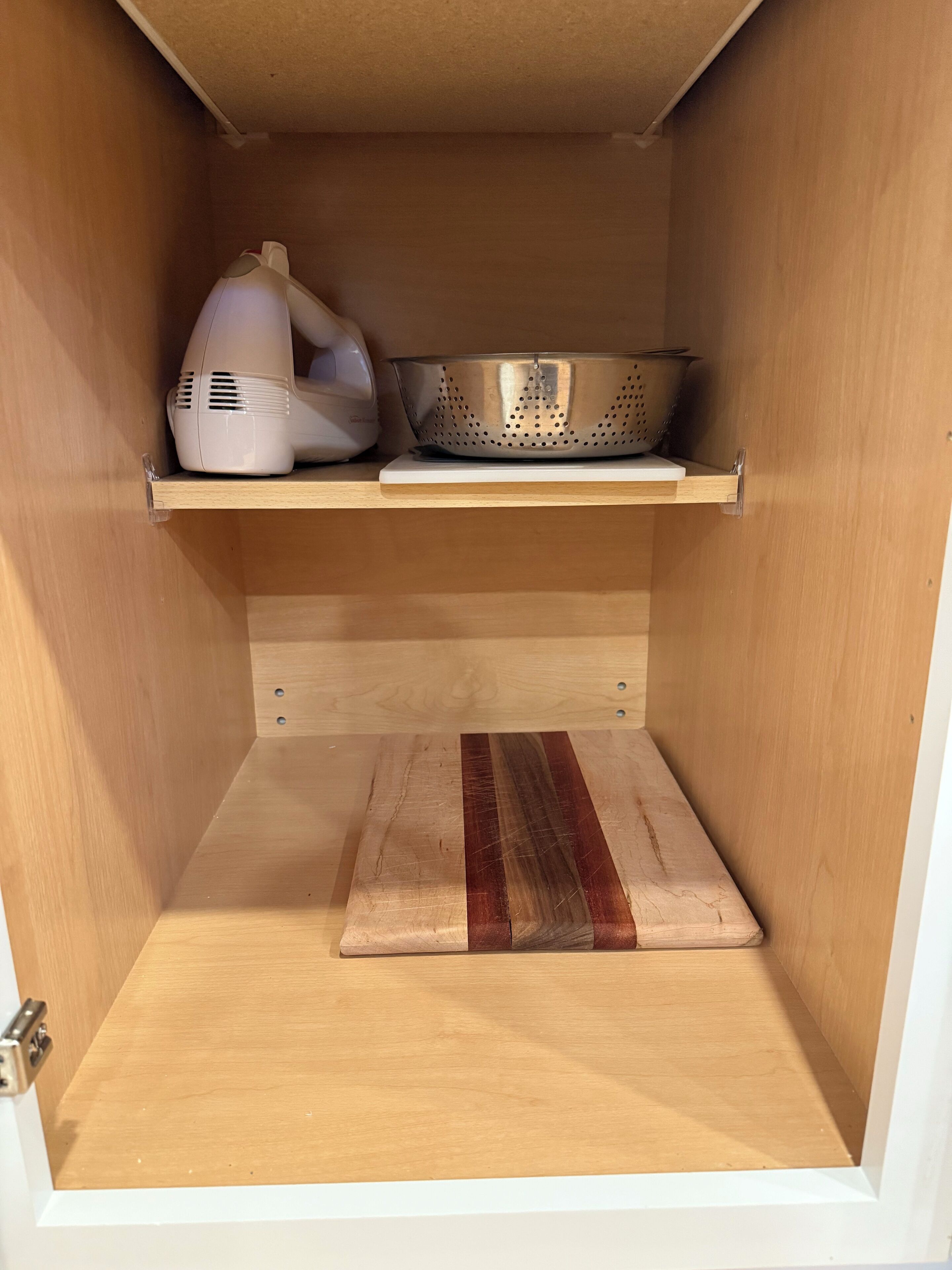 Un pensile da cucina con ripiano in legno che contiene una colapasta e un elettrodomestico bianco.