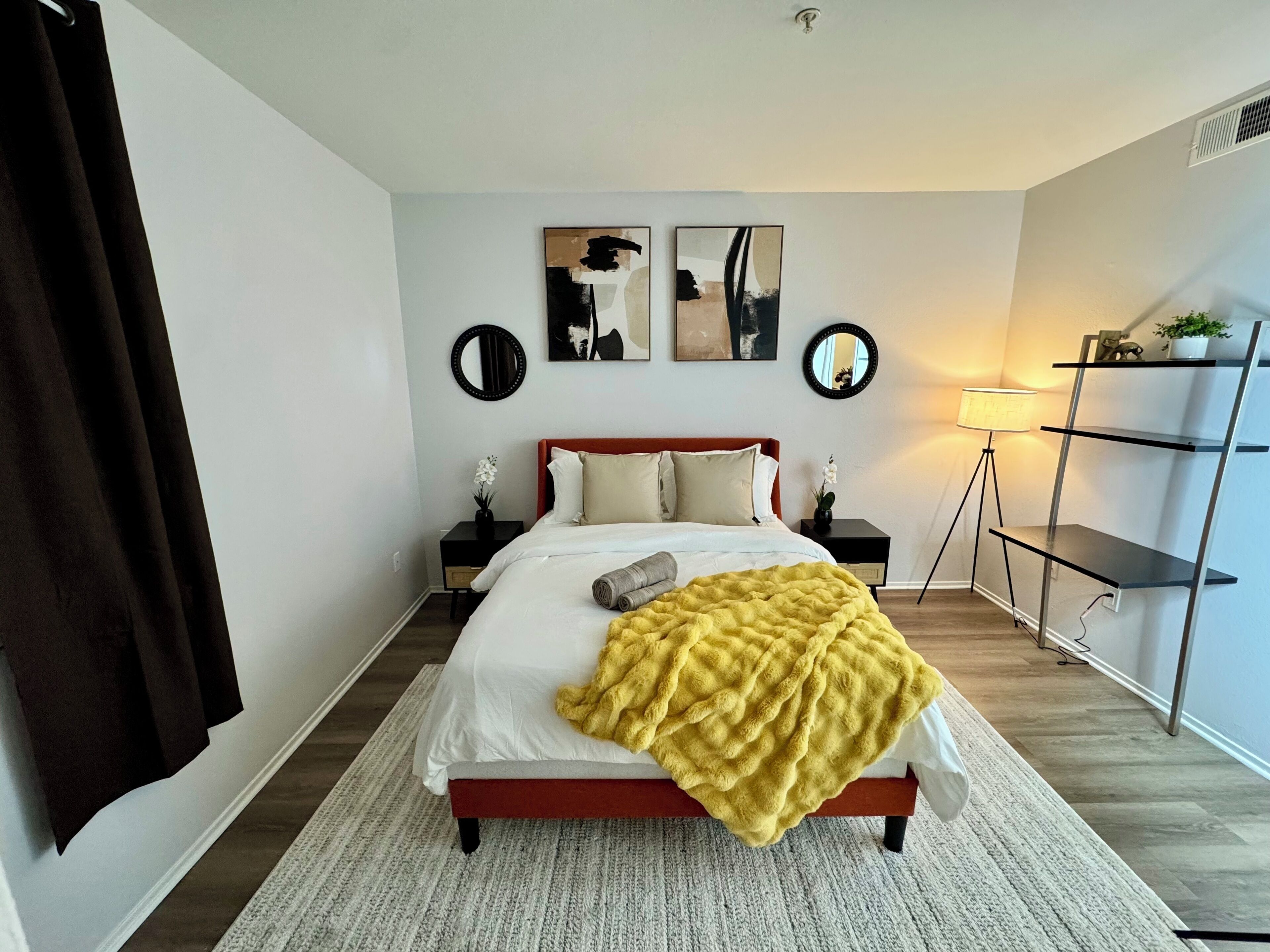 Une chambre à coucher comprenant un lit, deux tables de chevet, une lampe sur pied, une étagère et des œuvres d’art accrochées au mur.