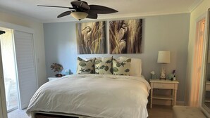 A bedroom with a bed, a nightstand, a lamp, a ceiling fan, and a painting of birds. - Stunning 2 bedroom, 2 balcony condo on golf course with tennis and pickleball (Naples)