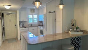 A modern kitchen with white cabinets, a central island with bar stools, a wine rack, and pendant lighting. - Stunning 2 bedroom, 2 balcony condo on golf course with tennis and pickleball (Naples)