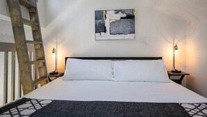 A neatly made bed with white linens, a modern abstract painting on the wall, and two bedside lamps.