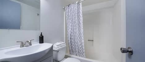 A modern bathroom with a white sink, mirror, toilet, and shower curtain.