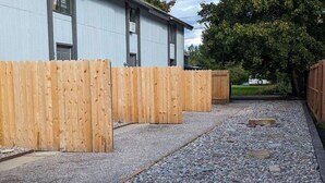 A gravel pathway leading to a wooden fence with a building in the background.