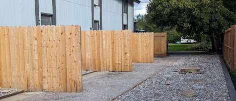 A gravel pathway leading to a wooden fence with a building in the background.