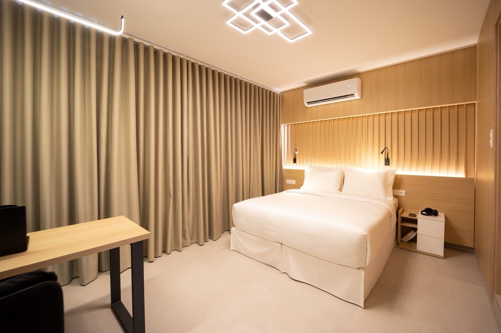 Een moderne hotelkamer met een bed, nachtkastje en bureau.