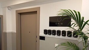 Un corridoio con una porta beige, una segnaletica per ÉRIA SUITES e una fila di oggetti neri su uno scaffale bianco.