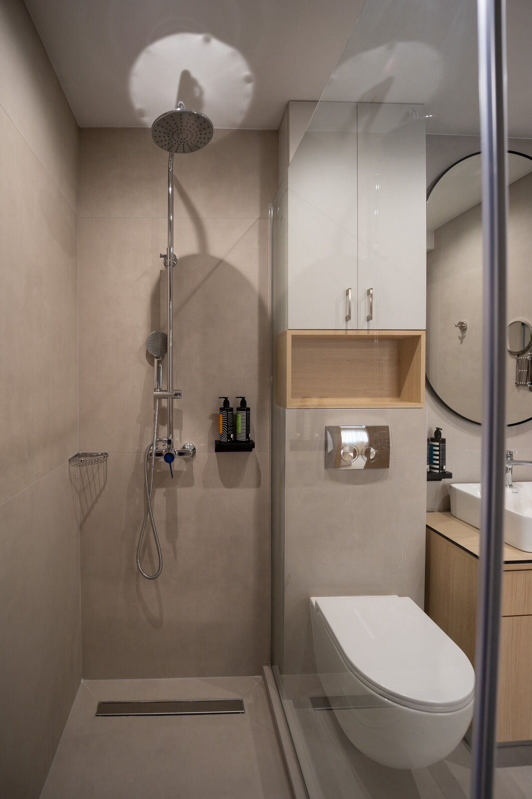 A modern bathroom with a glass-enclosed shower, a white toilet, and a wooden vanity with a mirror.
