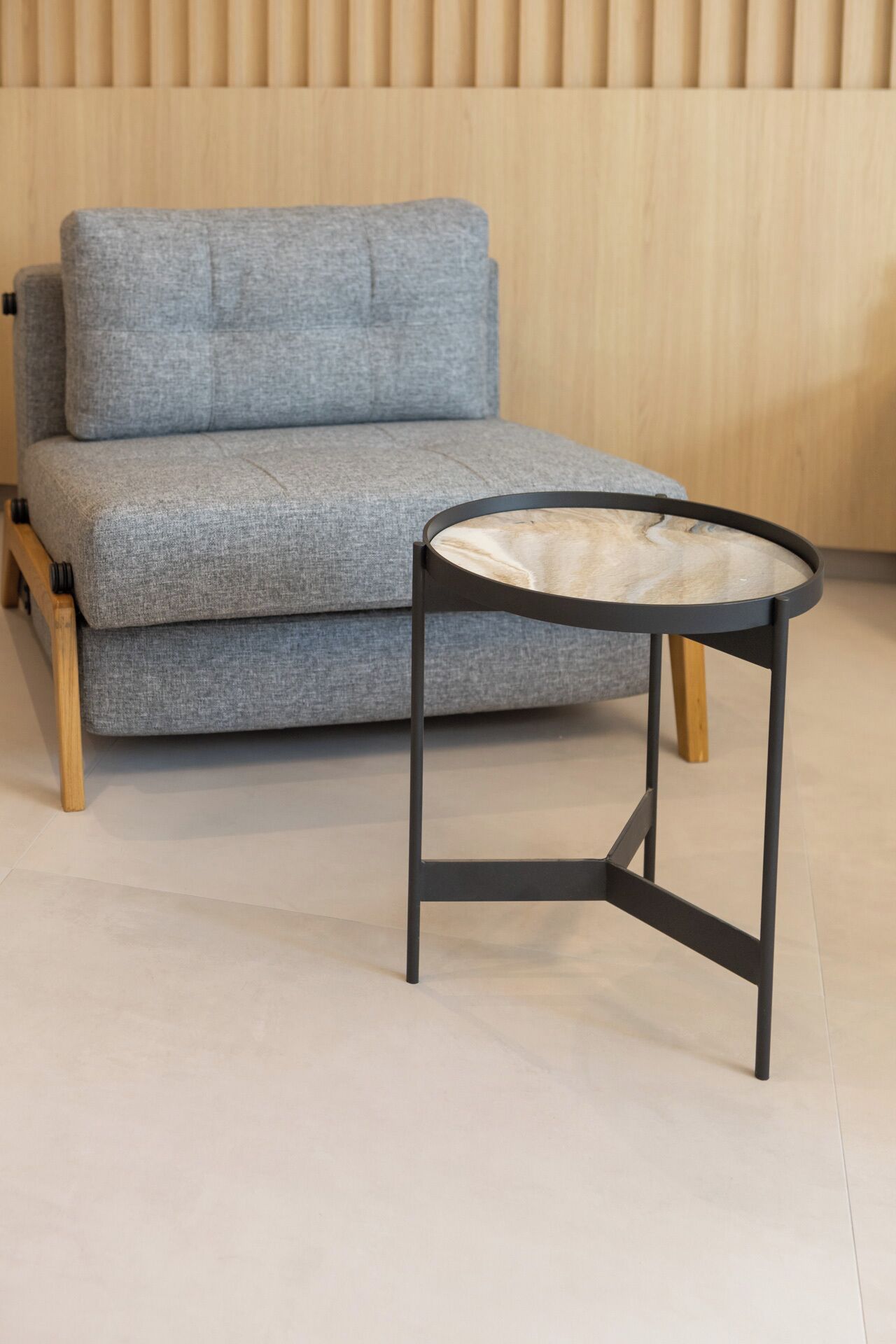 A grey sofa with wooden legs and a small round table with a wooden top and black metal frame.