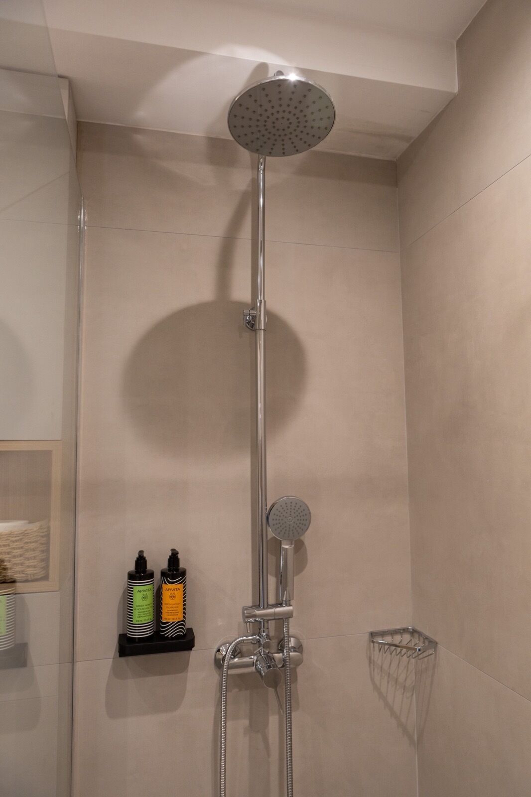Ducha con cabezal de ducha manual y grifo empotrado en la pared. Hay dos botellas en un estante debajo de la ducha.