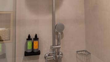 Ducha con cabezal de ducha manual y grifo empotrado en la pared. Hay dos botellas en un estante debajo de la ducha.