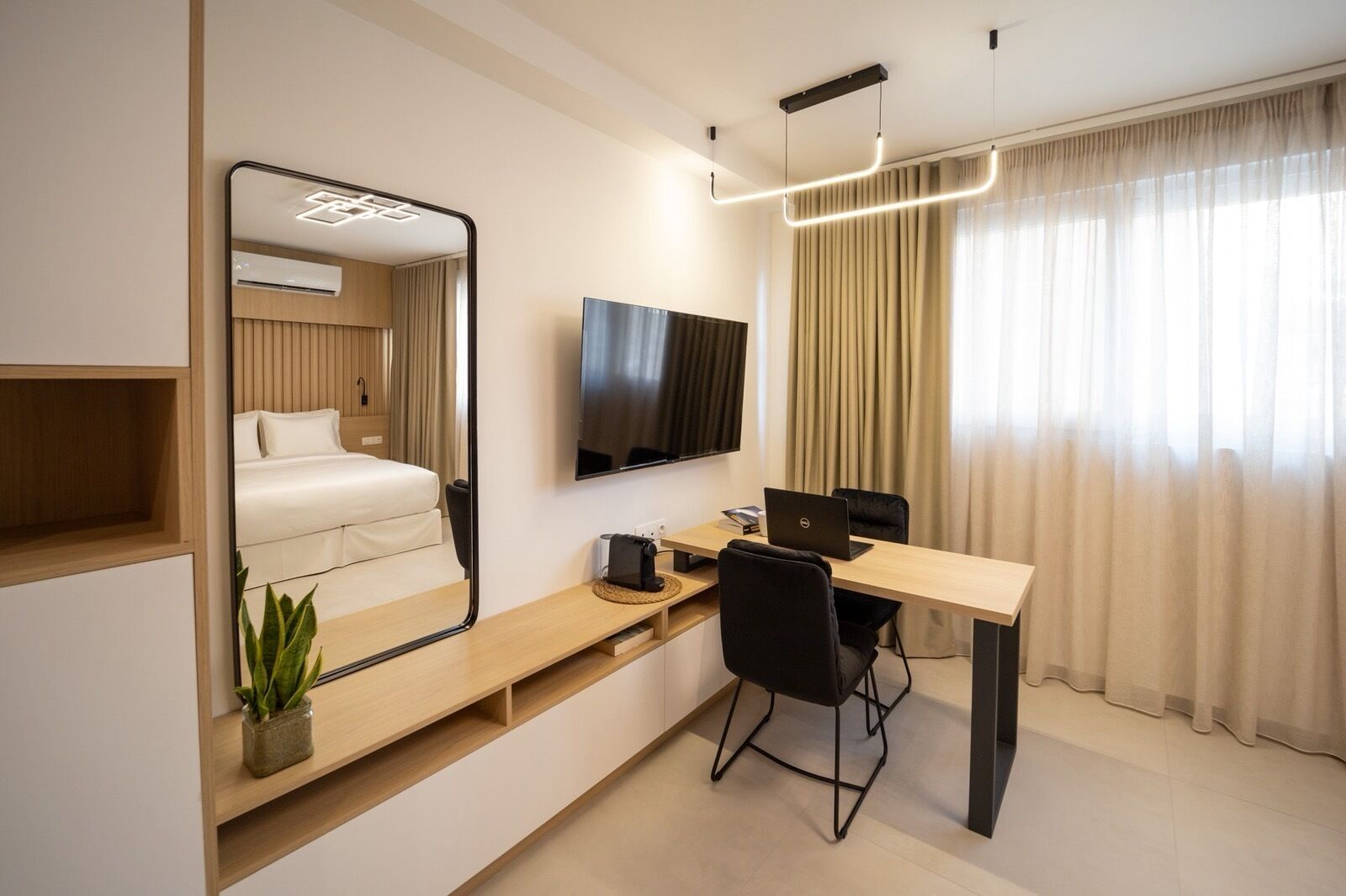 Habitación de hotel moderna con cama, escritorio, computadora portátil, televisor y un espejo grande.
