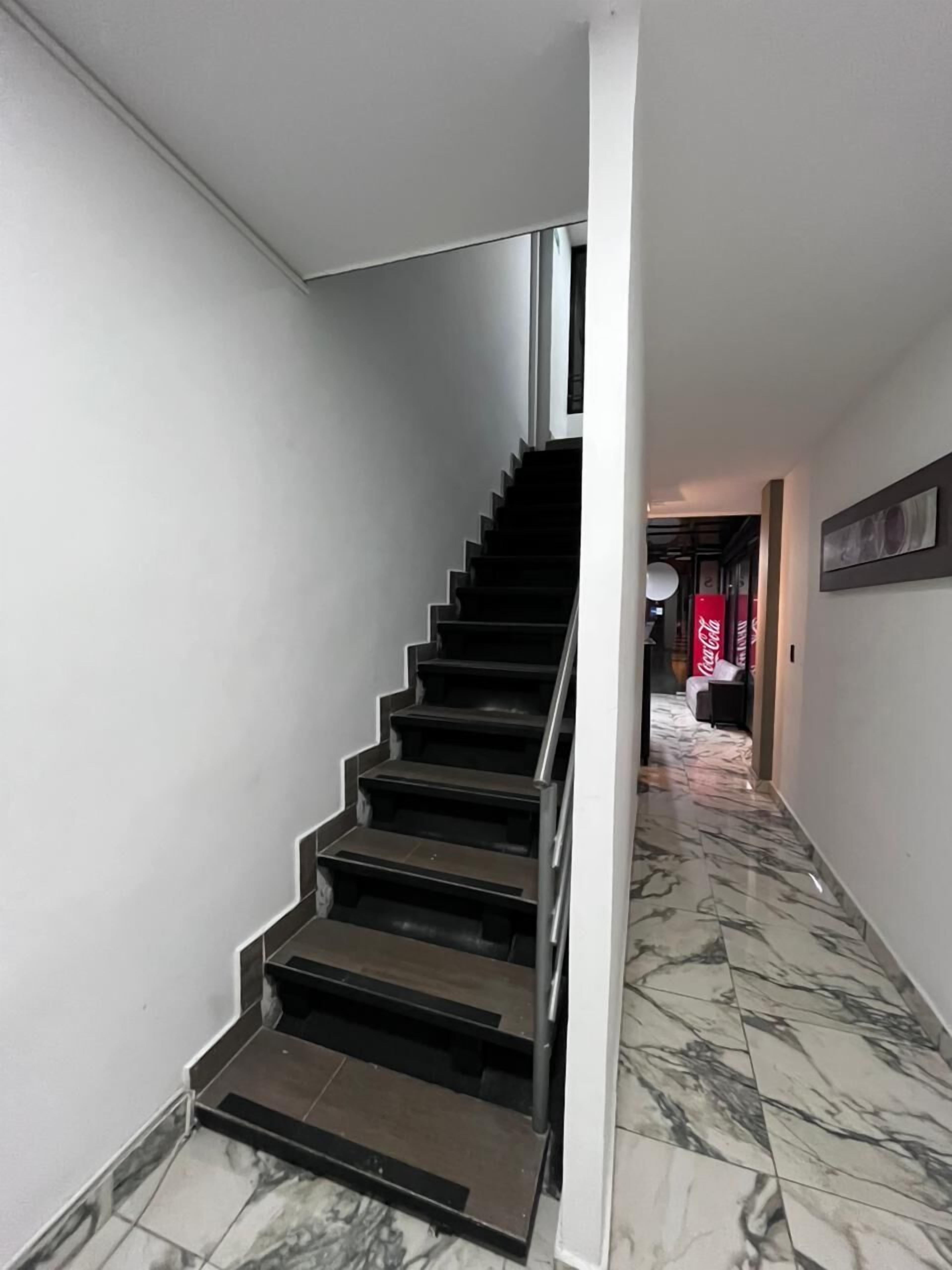 A modern staircase with a metal handrail, leading to a room with a bed and a red Coca-Cola sign.