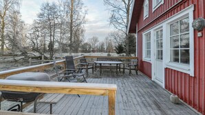 A wooden deck with a barbecue grill, outdoor seating, and a red building with large windows.