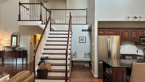 A spacious living area with a wooden staircase leading to an upper floor, a kitchen with modern appliances, and a cozy seating area. - Enjoy Derby City in this amazing river bungalow! (Louisville)