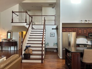 A spacious living area with a wooden staircase leading to an upper floor, a kitchen with modern appliances, and a cozy seating area.