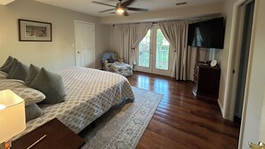 A bedroom with a bed, a ceiling fan, a television, and a door leading to a balcony. - Enjoy Derby City in this amazing river bungalow! (Louisville)