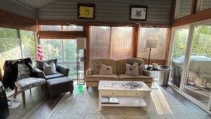 A spacious living room with a ceiling fan, a sofa set, a coffee table, and large windows. - Enjoy Derby City in this amazing river bungalow! (Louisville)