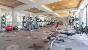 A spacious gym with various exercise equipment, large windows, and a wooden ceiling.