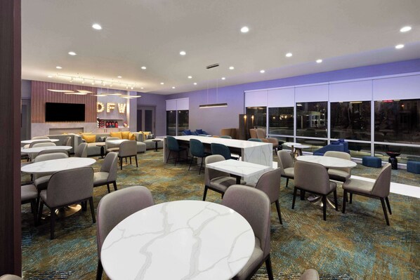 Un hall de hotel con mesas redondas, asientos cómodos, una zona de bar y ventanas amplias que ofrecen vistas.