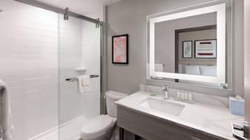 A modern bathroom with a glass shower enclosure, a white toilet, and a vanity with a large mirror.