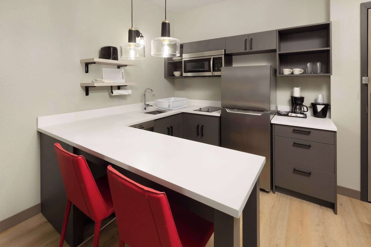 Una cocina moderna con una isla blanca, sillas rojas, electrodomésticos de acero inoxidable y lámparas colgantes negras.