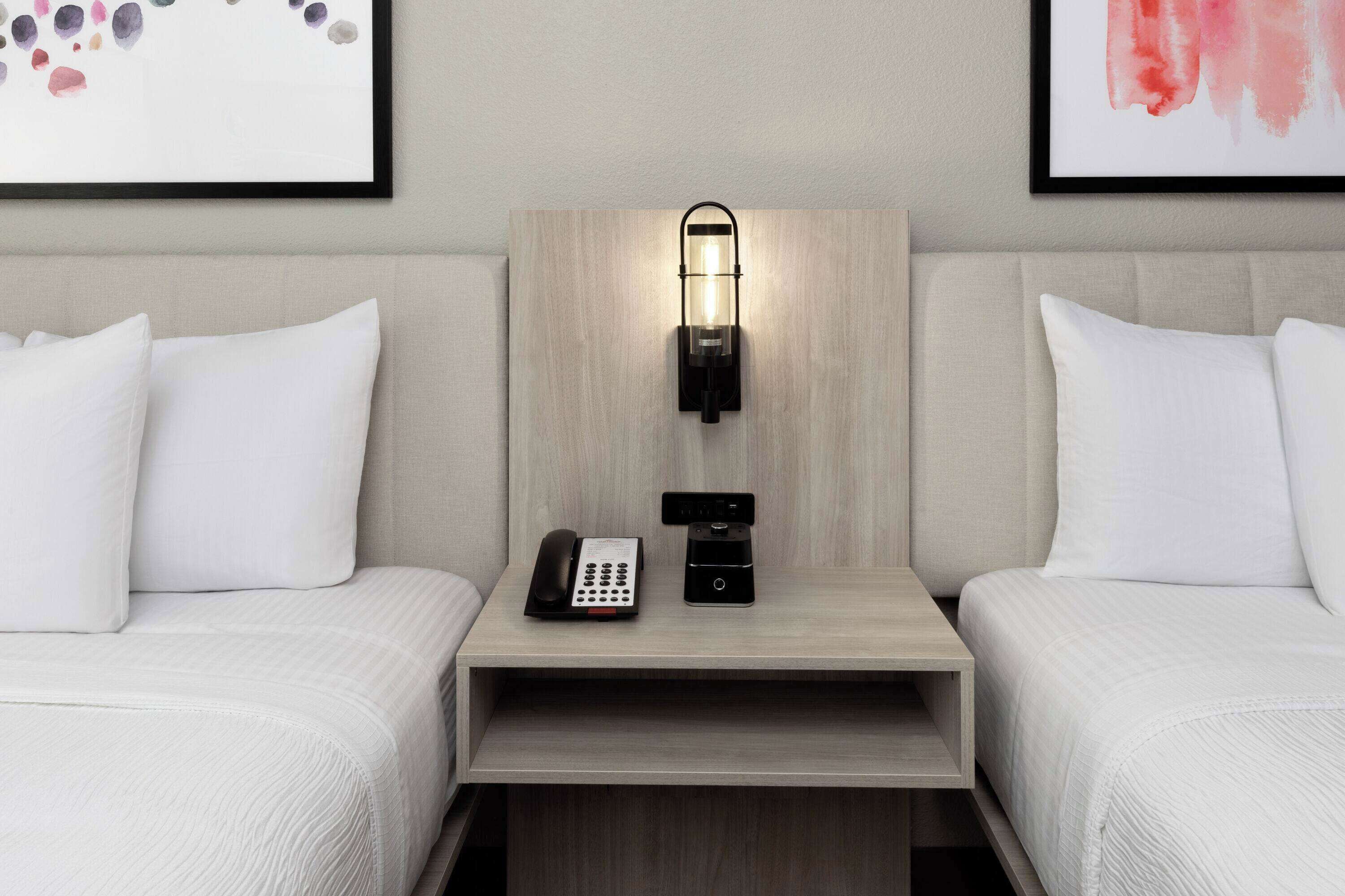 Una habitación de hotel con dos camas, una mesita de noche con lámpara, teléfono y cafetera.