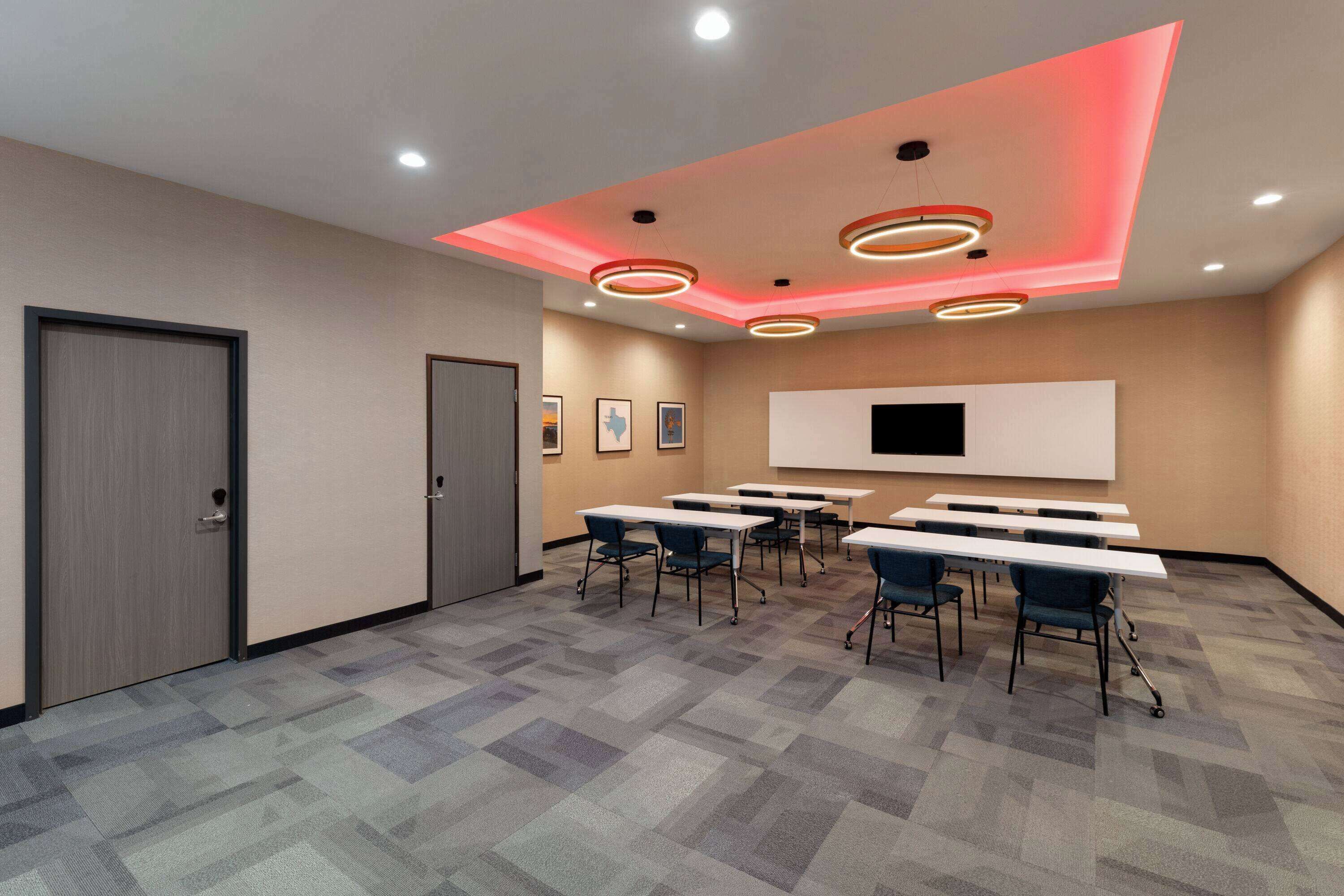 A conference room with a modern design, featuring a large whiteboard, multiple tables, and ceiling lighting.