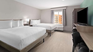 Ett hotellrum med två sängar, ett skrivbord, en TV och ett fönster med utsikt över staden.