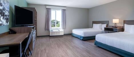 A hotel room with a desk, two beds, a TV, and a window with curtains.