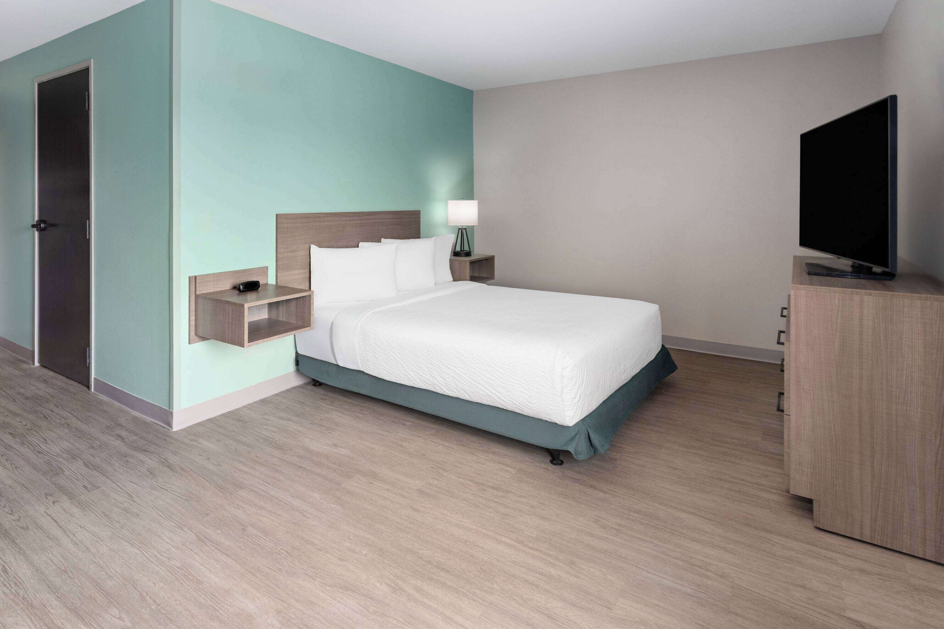 A hotel room with a bed, a TV, a nightstand, and a wardrobe.