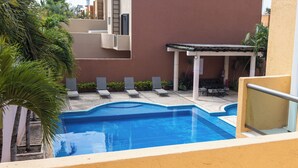 A swimming pool with lounge chairs, a covered seating area, and a building with a red facade. - Casa 25 Lizette Luxury for 6-7 px with Pool Cancun! (Cancún)