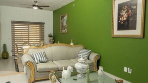 A living room with a green wall, a beige sofa with decorative pillows, a glass coffee table with figurines, and a ceiling fan. - Casa 25 Lizette Luxury for 6-7 px with Pool Cancun! (Cancún)