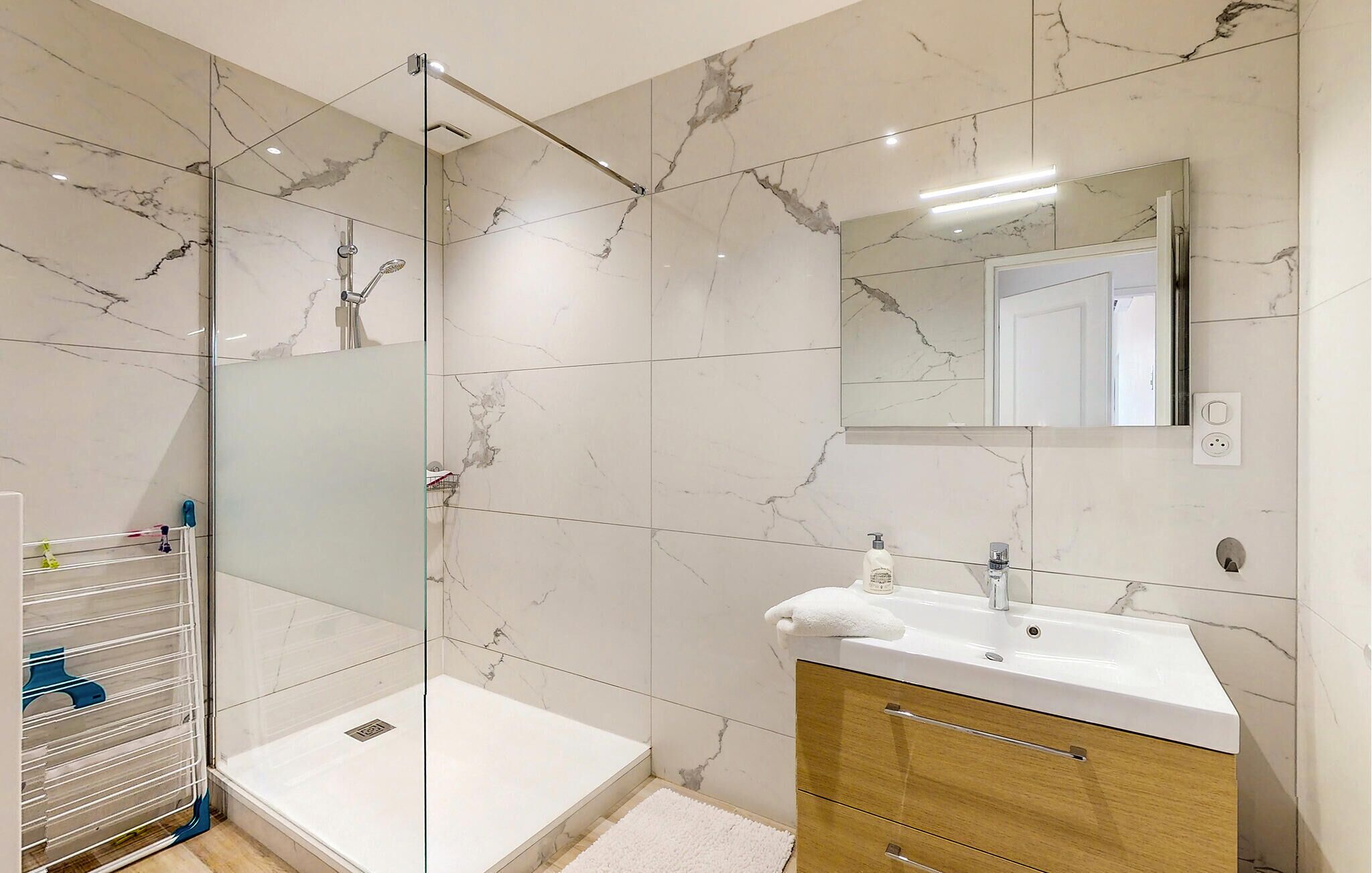 A modern bathroom with a glass-enclosed shower, a white sink, and a wooden vanity.