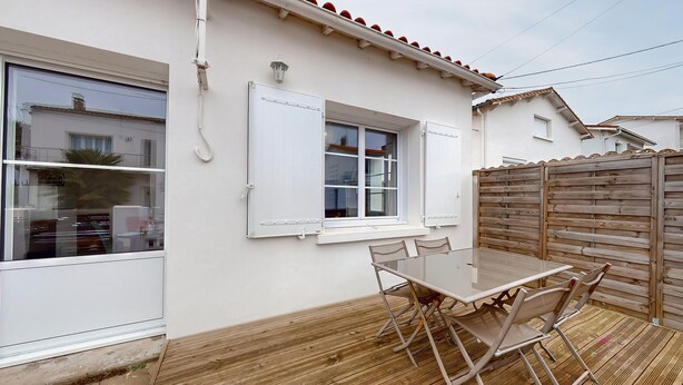 A patio with a glass table and chairs, a wooden fence, and a white building with windows and a door.