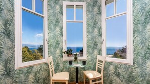 A corner room with three windows overlooking a coastal view, a small table with chairs, and tropical wallpaper. - Pet friendly apartment in Opatija with WiFi (Opatija)