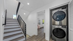 A modern interior with a staircase, a washing machine, and a bedroom with a bed and a window.
