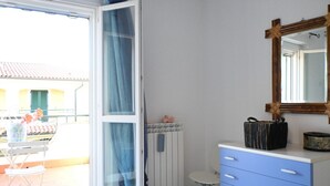Et værelse med en skydedør til en balkon, en hvid radiator, en blå kommode og et spejl med træramme.