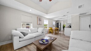 A spacious living area with a white sofa, a wooden coffee table, and a dining table with yellow chairs.