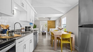 A modern kitchen with white cabinets, stainless steel appliances, and a wooden dining table with yellow chairs.