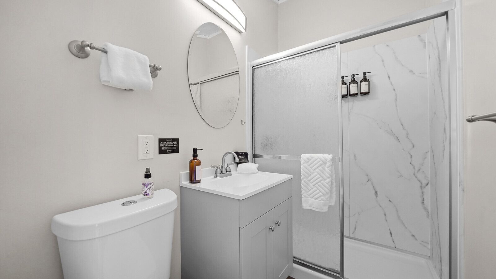 A modern bathroom with a toilet, sink, mirror, and shower.