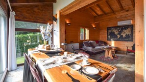Interior de una cabaña de madera con comedor listo para cuatro personas, un sofá y un mapa en la pared.