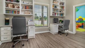 A home office with two desks, bookshelves, and a window with blinds.