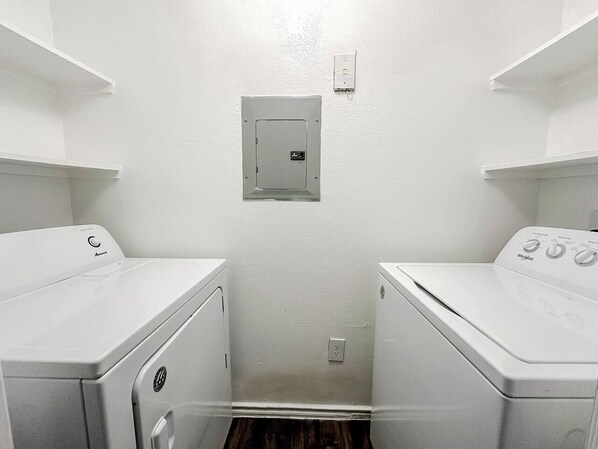 A laundry room with two front-loading washing machines and a utility panel on the wall.