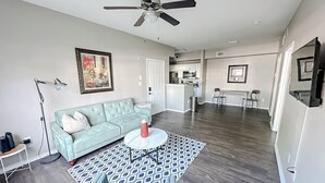 A spacious living area with a light blue sofa, a round coffee table, and a patterned rug. A ceiling fan is visible, and the room has hardwood flooring.